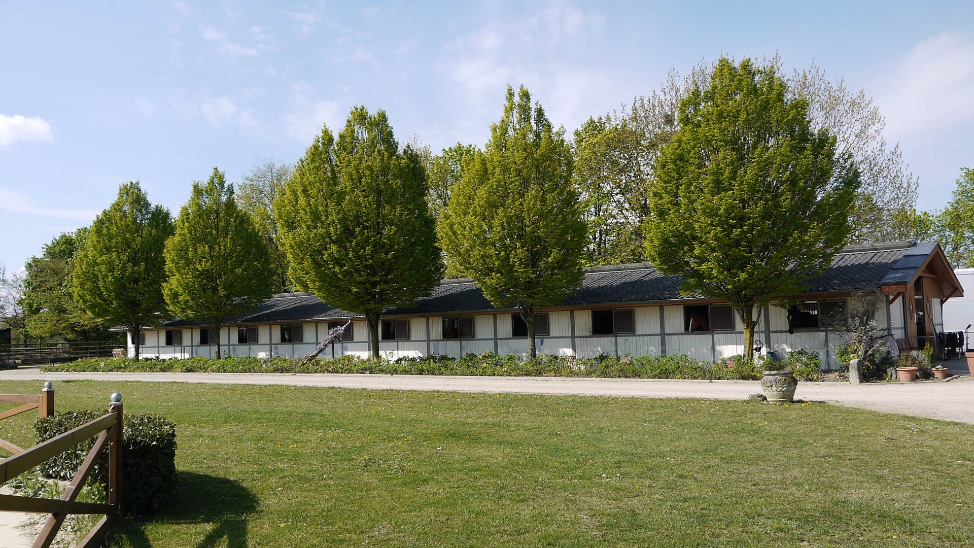 Ein langes, einstöckiges Gebäude mit weißer Fassade, vor dem grüne Bäume stehen.
