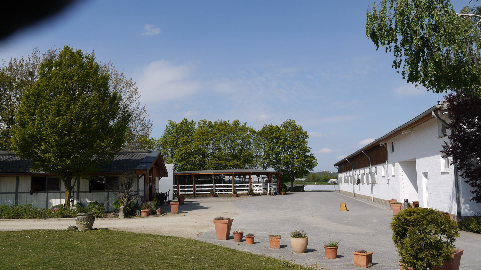 Ein leerer Hof mit weißen Gebäuden, Topfpflanzen und einem bewölkten blauen Himmel.